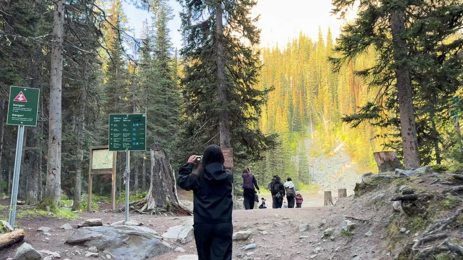 A hiker taking a photo beside trail signs in a pine forest, shown over the line “So choosing three things that matter the most to you”