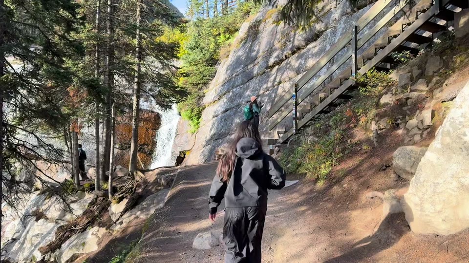 A hiker walking up a dirt path toward a small waterfall